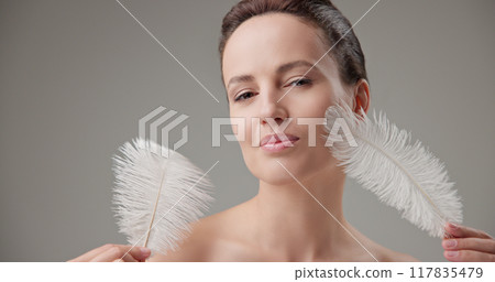 Beauty, health, cosmetics, anti-aging therapy and skin care concept - young beautiful brunette Caucasian woman holding a white fluffy feather, concept of tenderness, softness and lightness Beauty, health, cosmetics, anti-aging therapy and skin care concept - young beautiful brunette Caucasian woman holding a white fluffy feather, concept of tenderness, softness and lightness 117835479