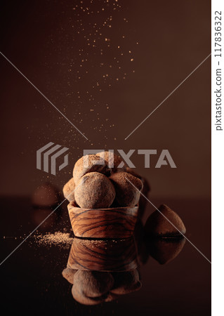 Chocolate truffles in small wooden dish sprinkled with cocoa powder. Black reflective background. 117836322