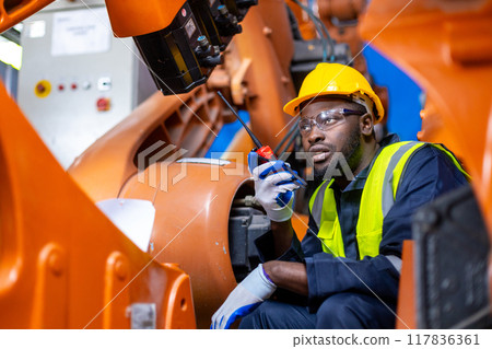 African American man engineer standing holding walkie talkie at automation robot arms African American man engineer standing holding walkie talkie at automation robot arms 117836361