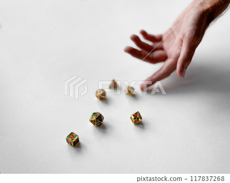 Hand reaching for colorful polyhedral dice on white surface Hand reaching for colorful polyhedral dice on white surface 117837268