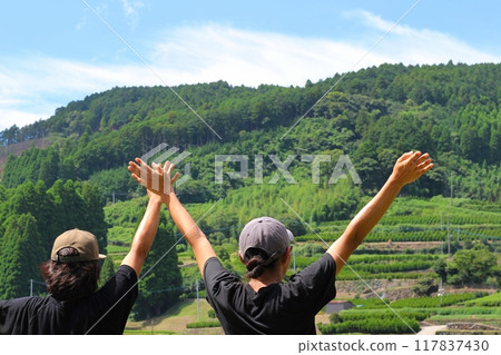 Two men looking at a mountain landscape with rice terraces, arms raised Two men looking at a mountain landscape with rice terraces, arms raised 117837430