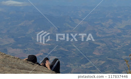 Person lying on a rock atop a mountain enjoying the view Person lying on a rock atop a mountain enjoying the view 117837446