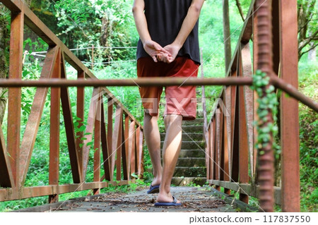 一個穿著短褲和涼鞋在綠山橋上行走的男人 117837550