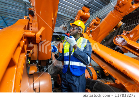 African American man engineer standing holding walkie talkie at automation robot arms African American man engineer standing holding walkie talkie at automation robot arms 117838272