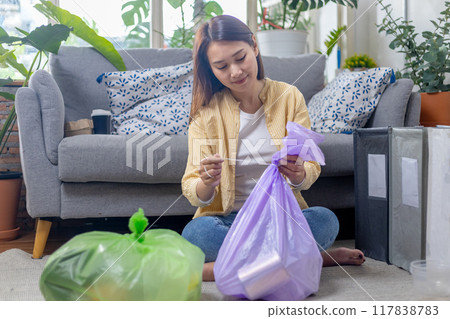 Young female sitting at home separating paper and plastic waste. Garbage sorting for recycle. Young female sitting at home separating paper and plastic waste. Garbage sorting for recycle. 117838783