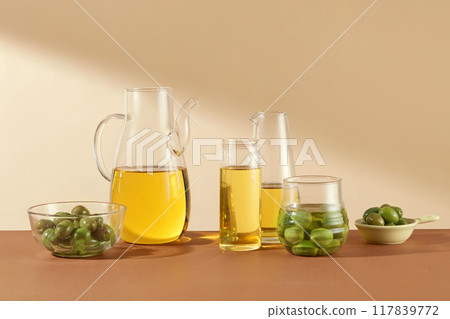 Front view of fresh olives decorated with glass flasks containing olive oil on beige background. Scene for display of organic cosmetic products with olive extract 117839772
