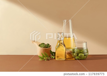 Minimal scene for advertising. Fresh olives, leaves and olive oil on glass bottles decorated on beige background. Front view, space for display product Minimal scene for advertising. Fresh olives, leaves and olive oil on glass bottles decorated on beige background. Front view, space for display product 117839773