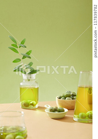 Advertising photo for olive ingredient. Fresh green olives decorated with glass flasks of olive oil on a green background. Front view, creative for advertising, space for display product 117839782