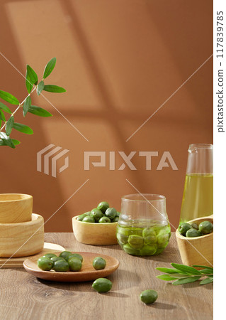 Front view of fresh green olives containing on wooden bowls decorated with leaves on brown background. Scene for advertising. Olive oil contains large amounts of antioxidants Front view of fresh green olives containing on wooden bowls decorated with leaves on brown background. Scene for advertising. Olive oil contains large amounts of antioxidants 117839785