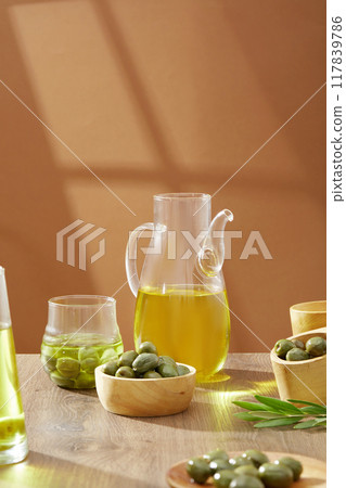 Olive oil is the natural oil extracted from olives, the fruit of the olive tree. Bowls of fresh green olives and flask of olive oil decorated on wooden table. Advertising photo 117839786