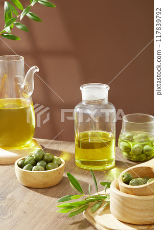 Wooden table with wooden bowls containing fresh olives decorated with a vase of olive oil and green leaves on a brown background. Vertical frame for social advertising Wooden table with wooden bowls containing fresh olives decorated with a vase of olive oil and green leaves on a brown background. Vertical frame for social advertising 117839792
