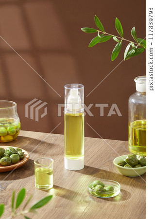 An empty bottle displayed on wooden table with fresh olives on bowls, olive oil and green leaves decorated on brown background. Mockup bottle unlabeled for design 117839793
