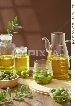 Advertising photo of nature ingredient for cosmetic product - olive. On wooden table and brown background, fresh olives decorated with glass bowls of olive oil Advertising photo of nature ingredient for cosmetic product - olive. On wooden table and brown background, fresh olives decorated with glass bowls of olive oil 117839795