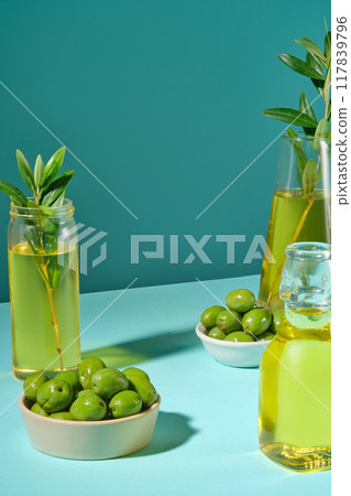 Fresh olives on ceramic bowls decorated with glass bottles of olive oil on green background. Advertising photo for cosmetic product with ingredients from olive Fresh olives on ceramic bowls decorated with glass bottles of olive oil on green background. Advertising photo for cosmetic product with ingredients from olive 117839796