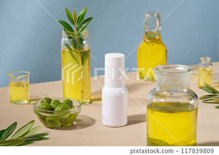 Template for cosmetic advertising with white bottle unlabeled displayed on blue background with fresh olives and glass bottles of olive oil. Olive extract concept Template for cosmetic advertising with white bottle unlabeled displayed on blue background with fresh olives and glass bottles of olive oil. Olive extract concept 117839809