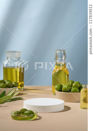 Pedestal for display cosmetic product of olive extract with white empty podium, fresh olives and olive oil on blue background. Olives contain many healthy nutrients Pedestal for display cosmetic product of olive extract with white empty podium, fresh olives and olive oil on blue background. Olives contain many healthy nutrients 117839812