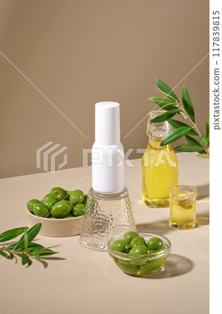 Bowls of fresh olives decorated with glass bottles of olive oil on light brown background. An empty white bottle displayed in the middle for design. Mockup bottle for advertising cosmetic 117839815
