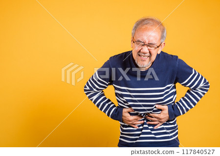 Portrait Asian old man with glasses holds hands on abdomen he stomach ache studio shot isolated yellow background, senior man pensioner feeling pain abdominal pain, hepatitis painful Portrait Asian old man with glasses holds hands on abdomen he stomach ache studio shot isolated yellow background, senior man pensioner feeling pain abdominal pain, hepatitis painful 117840527