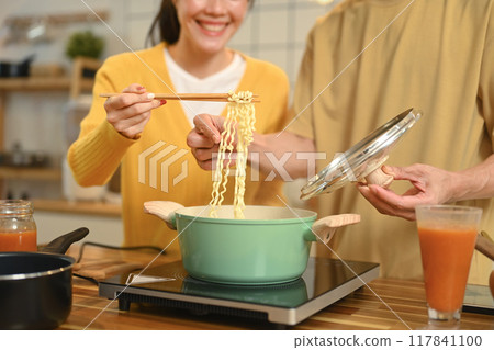 Happy young couple enjoying a casual meal in kitchen and sharing a bowl of instant noodles Happy young couple enjoying a casual meal in kitchen and sharing a bowl of instant noodles 117841100