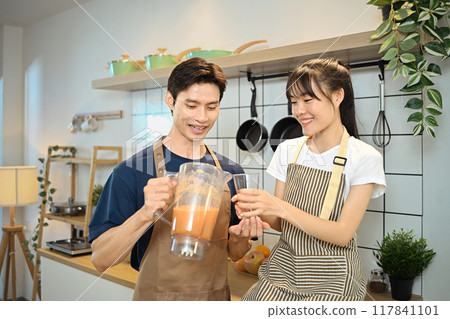Beautiful young couple wearing apron enjoying healthy fruit smoothie in domestic kitchen Beautiful young couple wearing apron enjoying healthy fruit smoothie in domestic kitchen 117841101