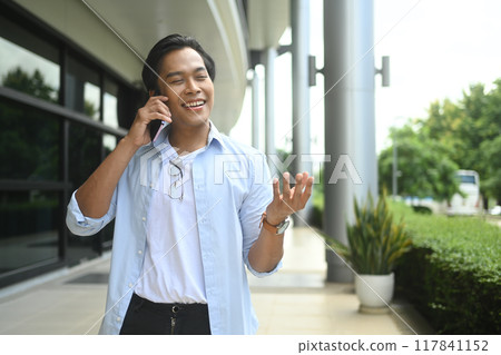 Young professional businessman talking on mobile phone outside a modern office building 117841152