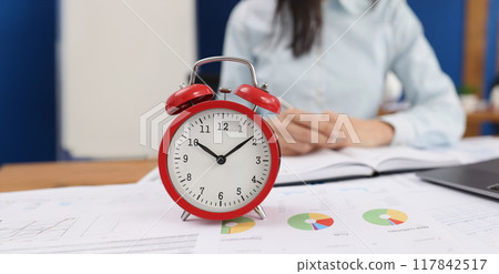 Red alarm clock on documents in the office, woman is blurry 117842517