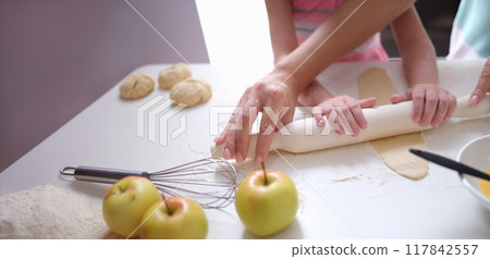 Mom and daughter roll out the dough with a rolling pin Mom and daughter roll out the dough with a rolling pin 117842557