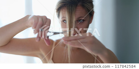 A woman scissors cuts her own hair, close-up A woman scissors cuts her own hair, close-up 117842584