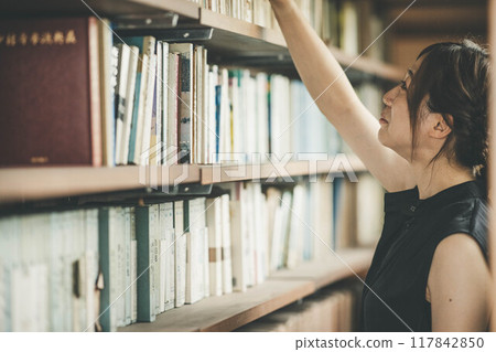 A young woman in a black dress trying to read a book 117842850