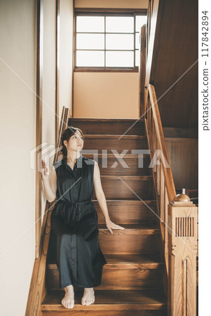 A woman in a black dress sitting on the stairs of an old house 117842894