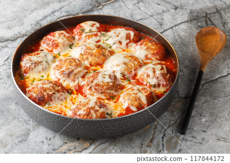 Italian casserole of baked meatballs in spicy tomato sauce with mozzarella cheese and thyme close-up in a baking dish. Horizontal 117844172