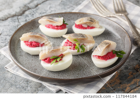 Spicy appetizer Stuffed eggs with beets and herring close-up in a plate. Horizontal 117844184