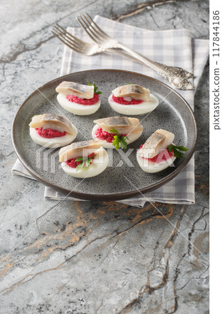 Hard-boiled eggs stuffed with beetroot salad and herring close-up in a plate. Vertical 117844186