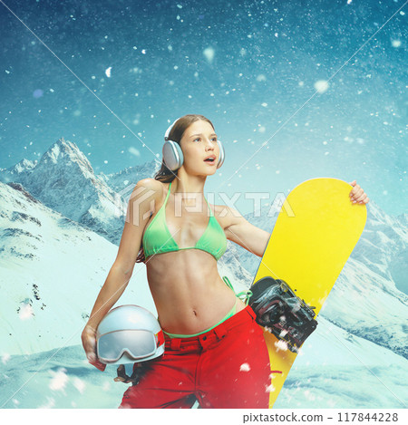 Young girl, snowboarder confidently posing with gear in winter landscape, dressed in bikini top, blending cold of winter with bold fashion statement. 117844228