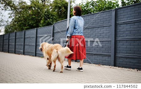 Girl Walks With Dog Along A Calm Street Girl Walks With Dog Along A Calm Street 117844502