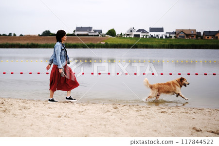 Playful Golden Retriever Runs And Plays With Its Female Owner On The Beach, Enjoying The Outdoors Playful Golden Retriever Runs And Plays With Its Female Owner On The Beach, Enjoying The Outdoors 117844522