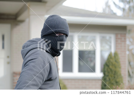 Masked man in front of suburban house 117844761