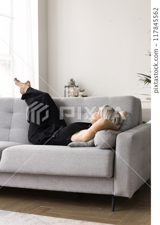 Satisfied peaceful mature female lying on sofa cushions 117845562
