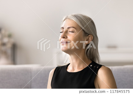 Woman closing her eyes resting seated on sofa at home 117845575