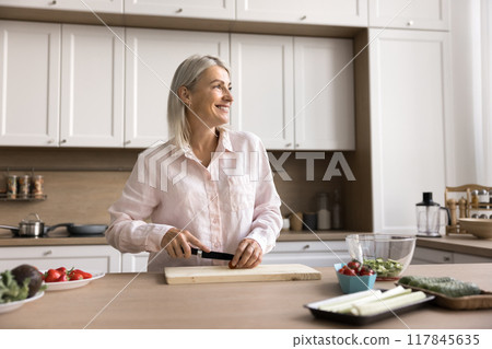 Happy mature 45s chef woman cooking salad at kitchen table 117845635