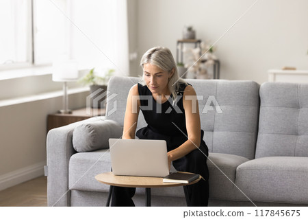 Focused serious woman working on laptop in living room 117845675