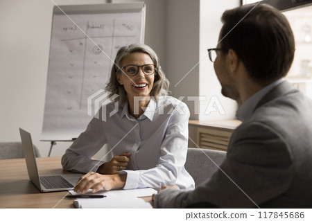 Happy mature woman negotiates with partner at conference table 117845686