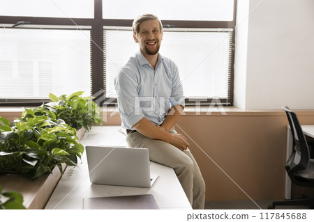 Office employee sits on table in coworking space with laptop 117845688