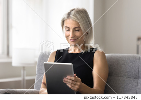 Middle aged woman relaxing at home with digital tablet 117845843