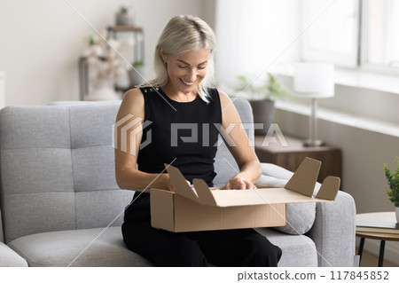 Woman sit on sofa open parcel box with bought goods Woman sit on sofa open parcel box with bought goods 117845852