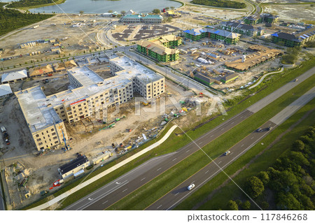 View from above of unfinished frame of apartment condos with wooden roof beams under construction. Development of residential housing near state highway in US suburbs. Real estate market in the USA 117846268