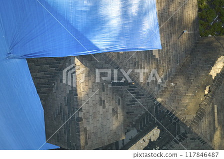 Top view of leaking house roof covered with protective tarp sheets against rain water leaks until replacement of asphalt shingles. Damage of building rooftop as aftermath of hurricane Ian in Florida 117846487