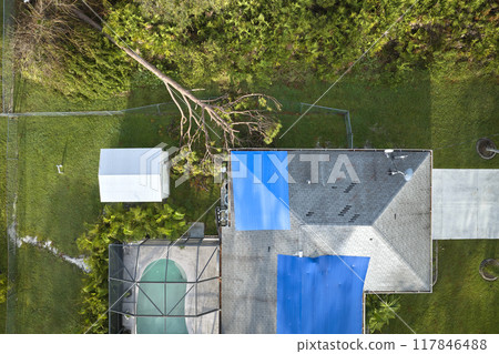Top view of leaking house roof covered with protective tarp sheets against rain water leaks until replacement of asphalt shingles. Damage of building rooftop as aftermath of hurricane Ian in Florida 117846488