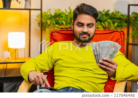 Rich happy Indian man counting money cash on smartphone calculator app, calculate income earnings 117846498