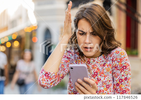 Surprised young woman use smartphone loses, bad news, fortune loss, fail outdoors in city street Surprised young woman use smartphone loses, bad news, fortune loss, fail outdoors in city street 117846526